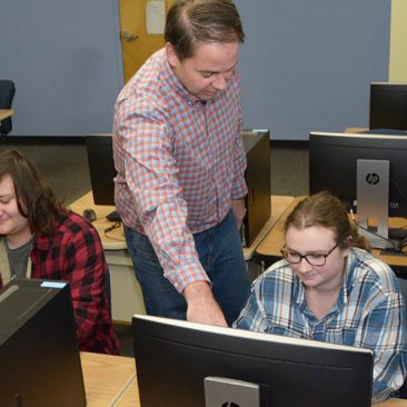 Professor working with students in computer lab classroom