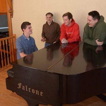 Professor with music students at a piano in Nordica auditorium performance hall