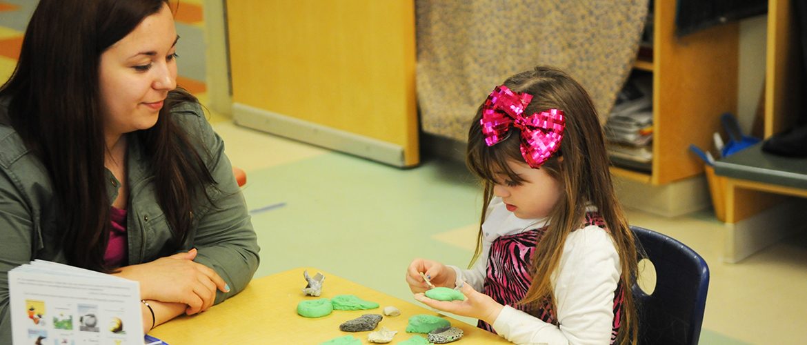 Woman-student working with preschool child on clay project