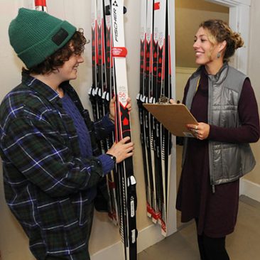 Student signing out skis to a patron at UMF Mainely Outdoors building