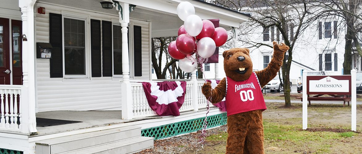 Beaver mascot holding balloons in front of admissions building