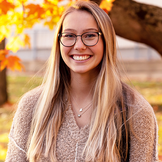 Female student in front of fall trees.