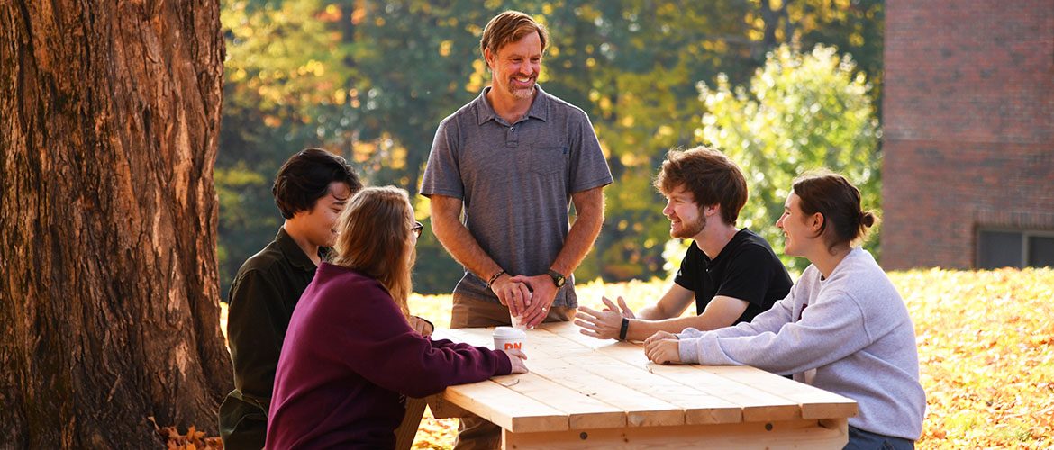 Students and a professor chatting at a picnic table
