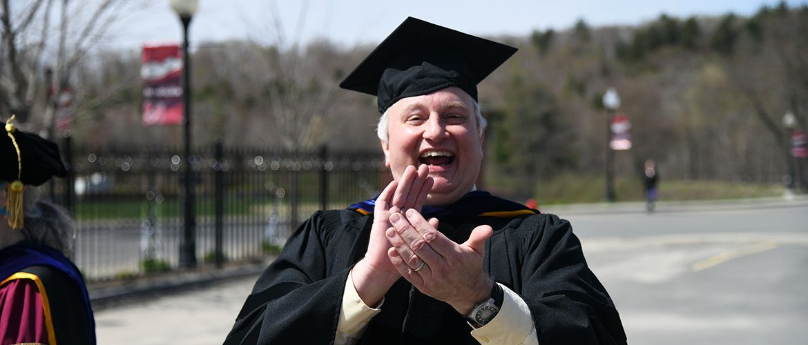 Professor in cap and gown applauding graduating students