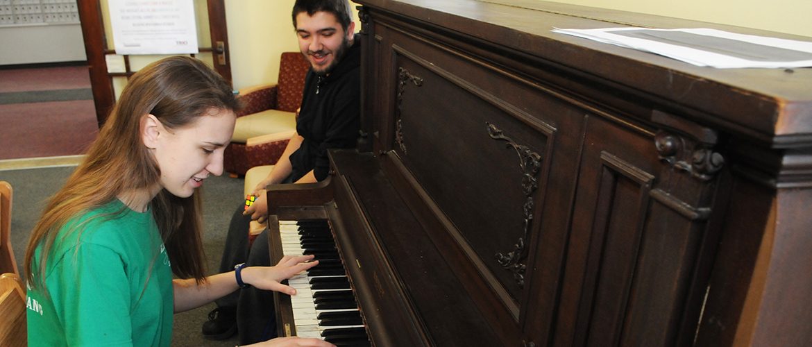 Students playing the piano in Mallett Hall's communal lounge area