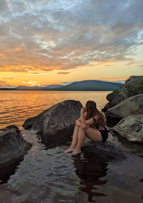 Student sitting on a rock in a lake, watching the sunset