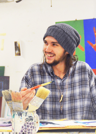 Student holding a paintbrush, smiling at something off-camera