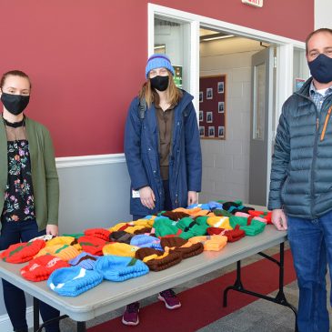 (Left to right) Brianna Hinkley, UMF senior from Kingfield and Peer Care Manager at UMF Covid Testing sight helps Page Brown, UMF senior from Boothbay, select her favorite hat from a huge assortment, with Keenan Farwell, director of UMF Facilities Management.